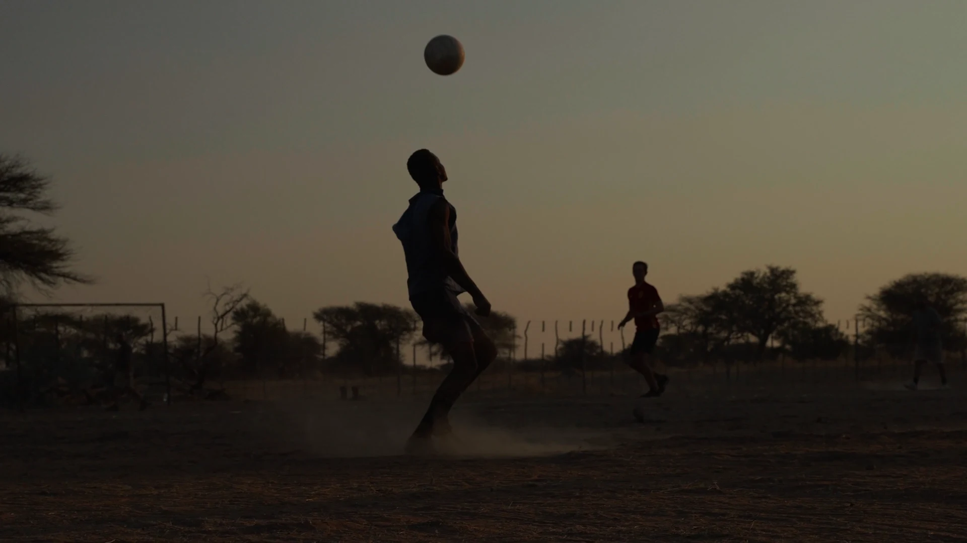 Fußball auf einem staubigen Platz im Abendlicht.
